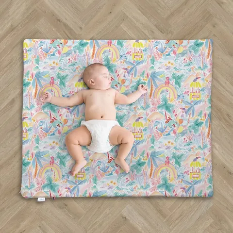 Bébé en couche allongé sur le dos au centre du tapis Jungle enchantée, parquet en chevrons, vue du dessus
