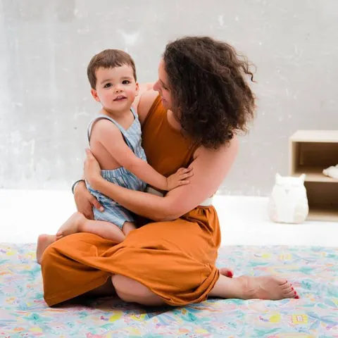 Femme assise qui serre un jeune enfant dans ses bras sur le tapis à jungle aquarelle pastel