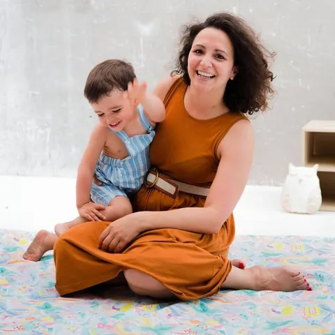 Une maman souriante et son enfant sur ses genoux, sur le Tapis Magique Jungle enchantée