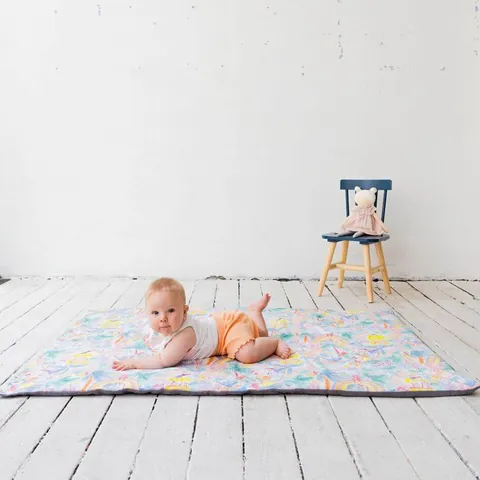 Bébé sur le ventre qui regarde l'objectif sur le tapis à jungle aquarelle pastel, plancher blanc, chaise en fond