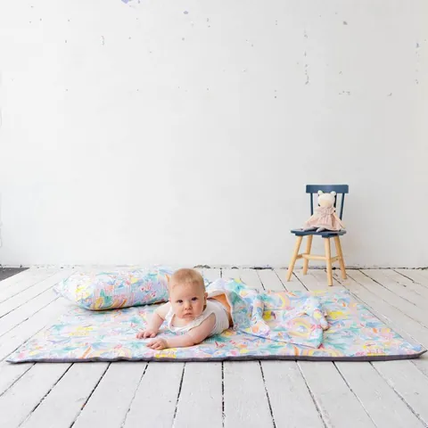 Bébé sur le ventre sur le tapis à jungle aquarelle pastel avec coussin et couverture assortis, plancher blanc