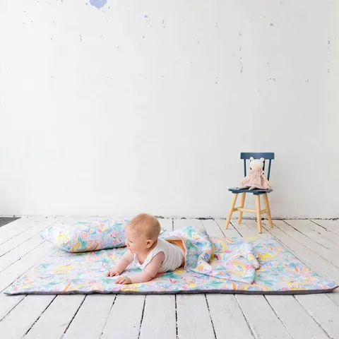 Bébé sur le ventre sur le tapis Jungle enchantée avec son coussin, plancher blanc, chaise en fond