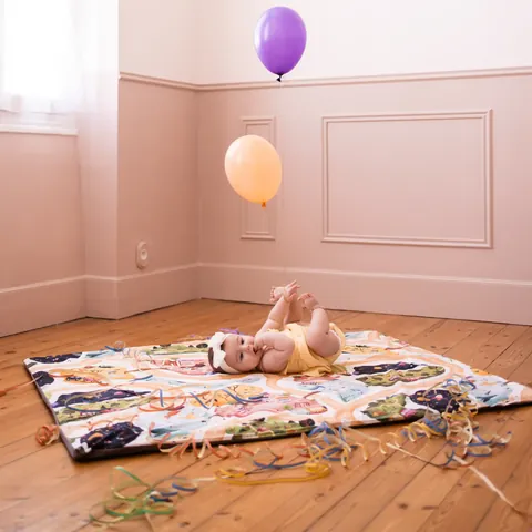 Plan large : bébé sur le tapis À la croisée des mondes au milieu d'une chambre rose, ballons et parquet