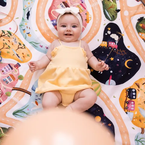 Bébé souriant en barboteuse jaune, allongé sur le Tapis Magique À la croisée des mondes