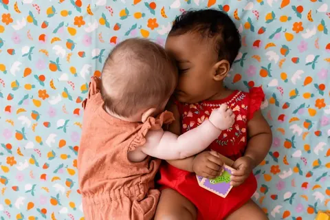 Deux bébés joue contre joue sur le tapis bleu clair à confettis colorés, gros plan