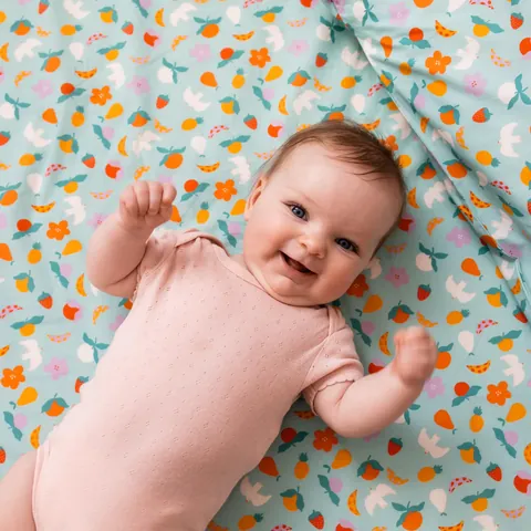 Bébé souriant en body rose allongé sur l'imprimé Pique-nique, coussin assorti, vue du dessus