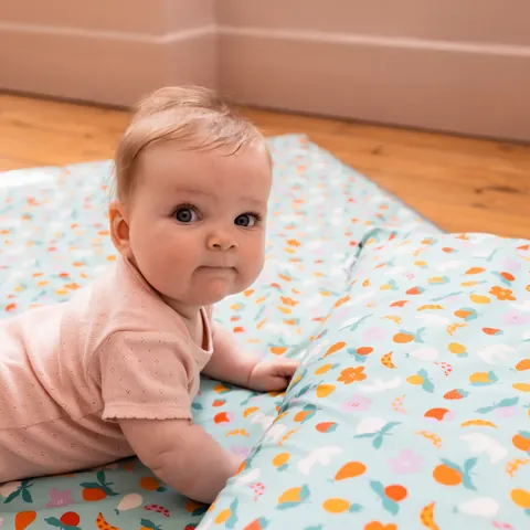 Bébé sur le ventre qui regarde l'objectif, tapis Pique-nique et parquet, murs roses