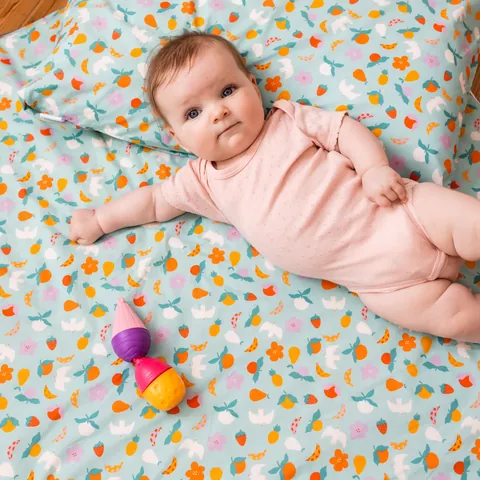 Bébé en body rose allongé sur le tapis Pique-nique avec coussin et jouet coloré, vue du dessus
