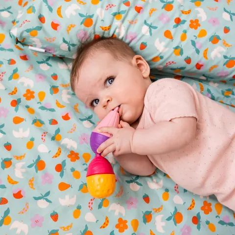 Bébé sur le côté qui mordille un jouet coloré sur l'imprimé Pique-nique, coussin derrière