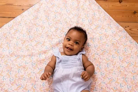 Bébé souriant allongé sur le tapis rose pâle à petites fleurs, vue de dessus