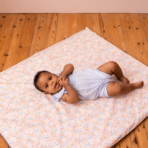 Bébé allongé sur le côté, main à la bouche, sur le tapis Poésie posé sur un parquet