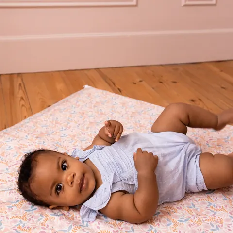 Bébé souriant allongé sur le tapis rose pâle à petites fleurs, plan rapproché au ras du sol
