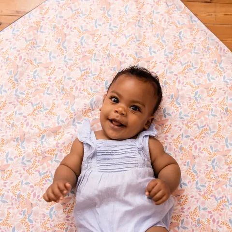 Bébé souriant en barboteuse bleu ciel, allongé sur le Tapis Magique Douce poésie