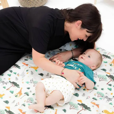 Femme penchée sur un bébé allongé sur le tapis crème à girafes et zèbres