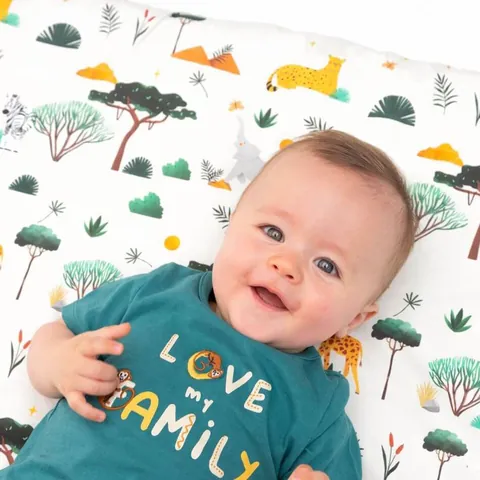 Bébé souriant allongé sur le tapis crème à animaux de savane, gros plan