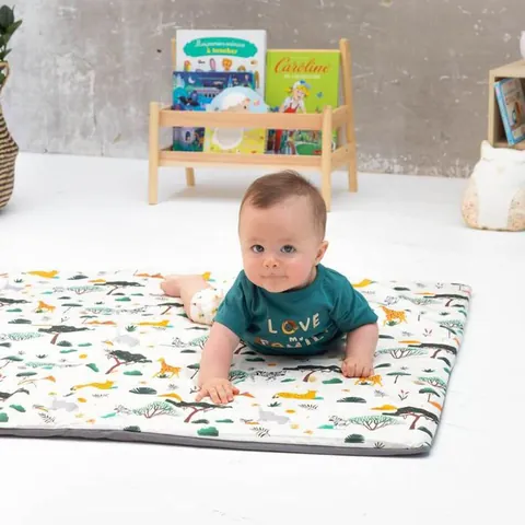 Bébé sur le ventre sur le tapis crème à animaux de savane, étagère à livres en fond
