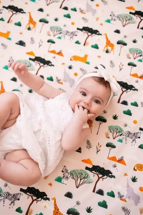 Bébé au bandeau blanc qui suce son doigt, allongé sur le tapis crème à girafes et zèbres, vue de dessus
