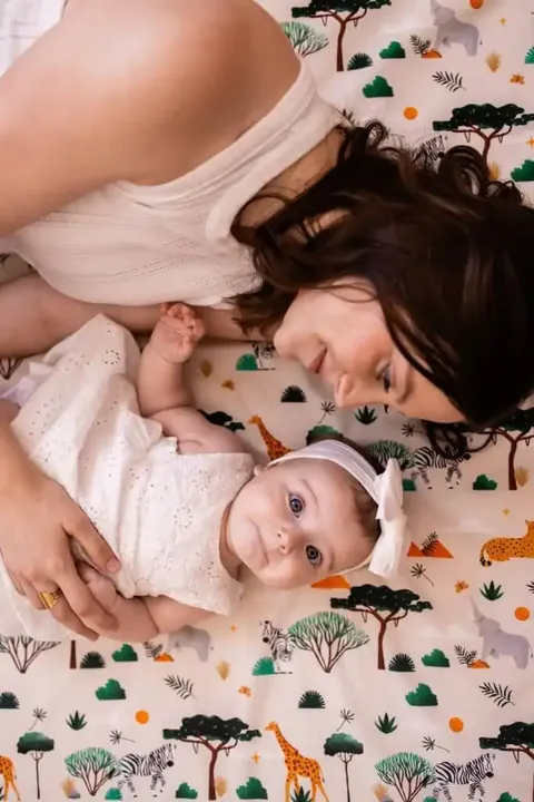 Mère allongée tête contre tête avec un bébé sur le tapis crème à girafes et zèbres, vue de dessus