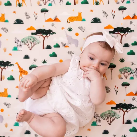 Bébé qui attrape son pied, allongé sur l'imprimé Savane, bandeau à noeud, vue du dessus