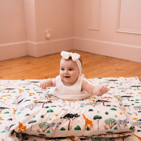 Bébé souriant au bandeau blanc sur le ventre sur le tapis Savane, murs roses et parquet
