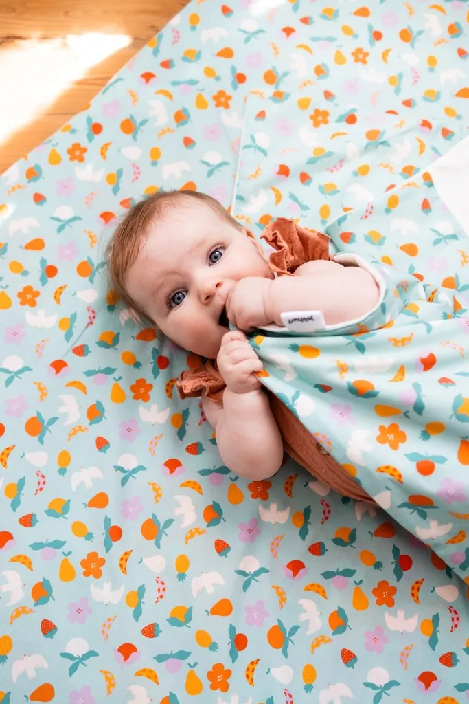 Un bébé à quatre pattes sur le Tapis Magique imprimé Pique-nique estival, la couverture assortie posée sur l'épaule.