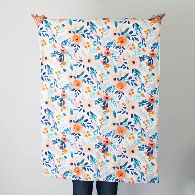 Gros plan sur un coton imprimé de fleurs pêche et bleues, tenu à bout de bras