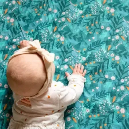 Vue de dessus d’un bébé coiffé d’un bandeau noué, à plat ventre sur un tapis vert d’eau à feuillages
