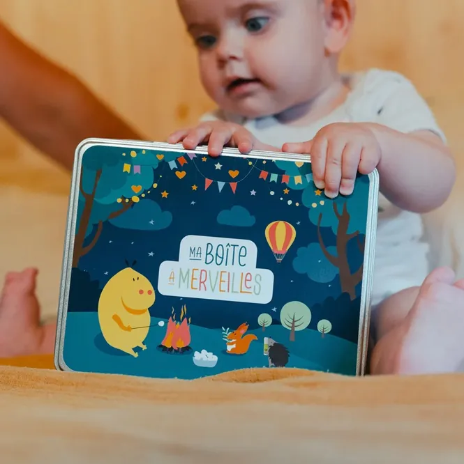 Un bébé assis qui tient une boîte illustrée « Ma boîte à merveilles »