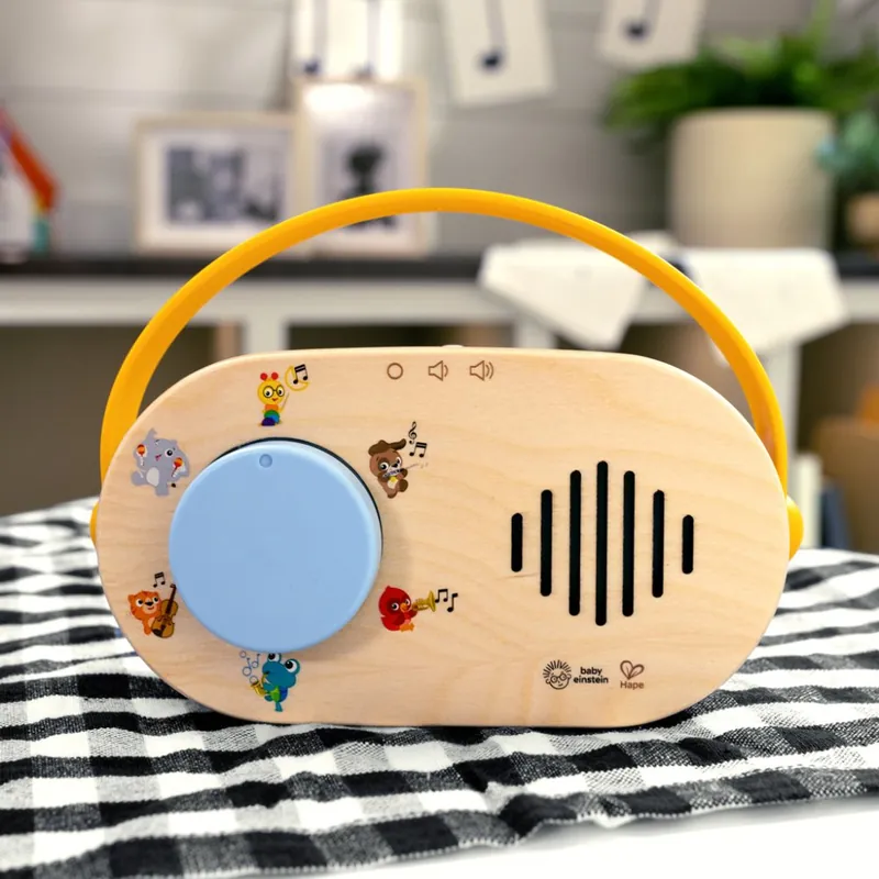 Une radio en bois pour enfant, à poignée jaune et bouton bleu, posée sur une nappe à carreaux noirs et blancs