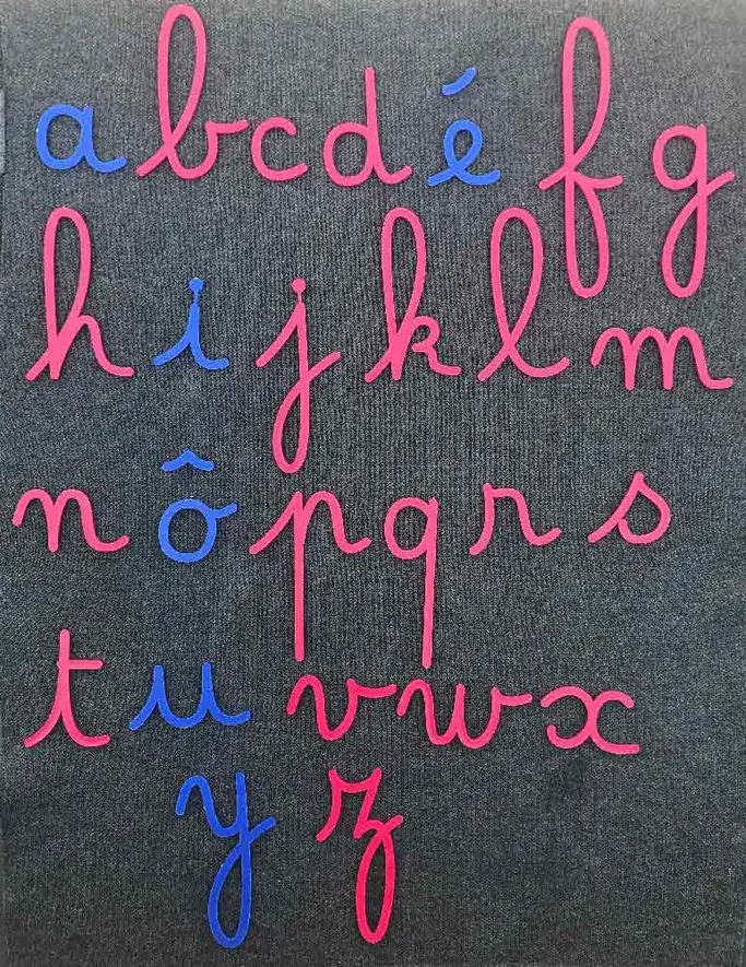 Les lettres de l’alphabet en écriture cursive, voyelles en bleu et consonnes en rose, disposées sur un fond gris foncé