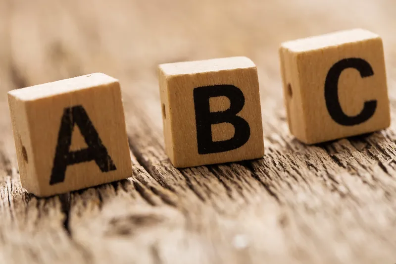 Trois cubes en bois marqués des lettres A, B et C, posés sur une planche en bois
