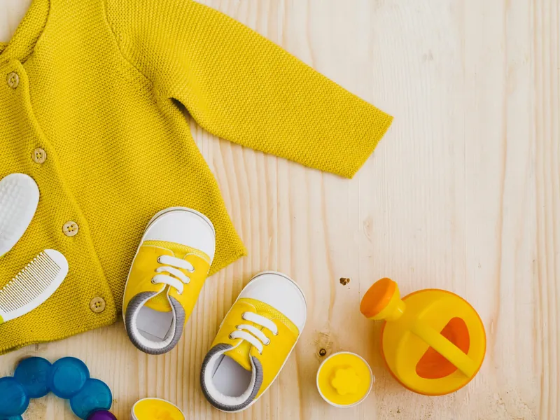 Un gilet en maille jaune, une paire de baskets jaunes et des jouets posés sur un plancher en bois clair