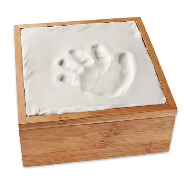 L'empreinte d'une main de bébé moulée dans une plaque blanche, dans un cadre en bois