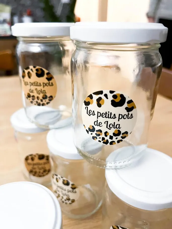 Des petits pots en verre à couvercle blanc, étiquetés « Les petits pots de Lota » sur fond léopard