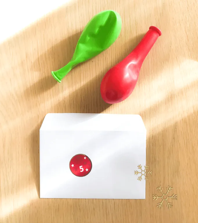 Deux ballons de baudruche dégonflés, un vert et un rouge, au-dessus d'une enveloppe blanche marquée d'une gommette 5