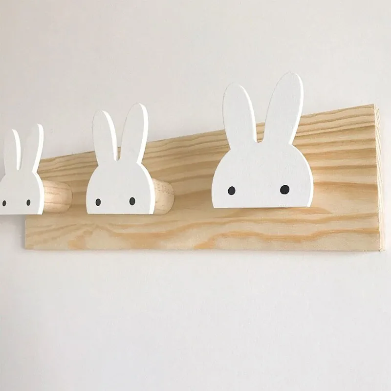 Un porte-manteau mural en bois clair aux crochets blancs en forme de tête de lapin