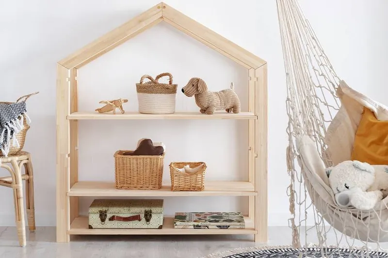 Une étagère en bois en forme de maison, garnie de paniers en osier et de jouets, à côté d'un hamac en macramé