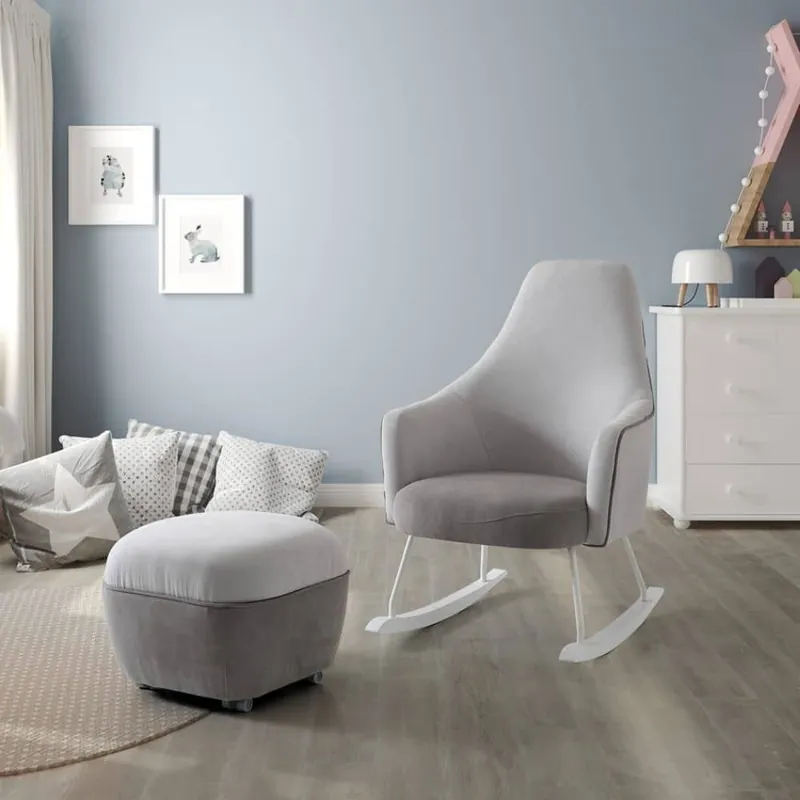 Un fauteuil à bascule gris et son repose-pieds devant un mur bleu gris, à côté d'une commode blanche
