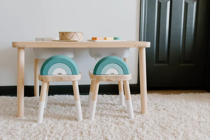 Une table basse en bois et deux tabourets d'enfant en arc-en-ciel sur un tapis blanc