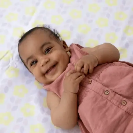 Un bébé souriant allongé sur un tissu imprimé de fleurs jaunes, les mains près du visage