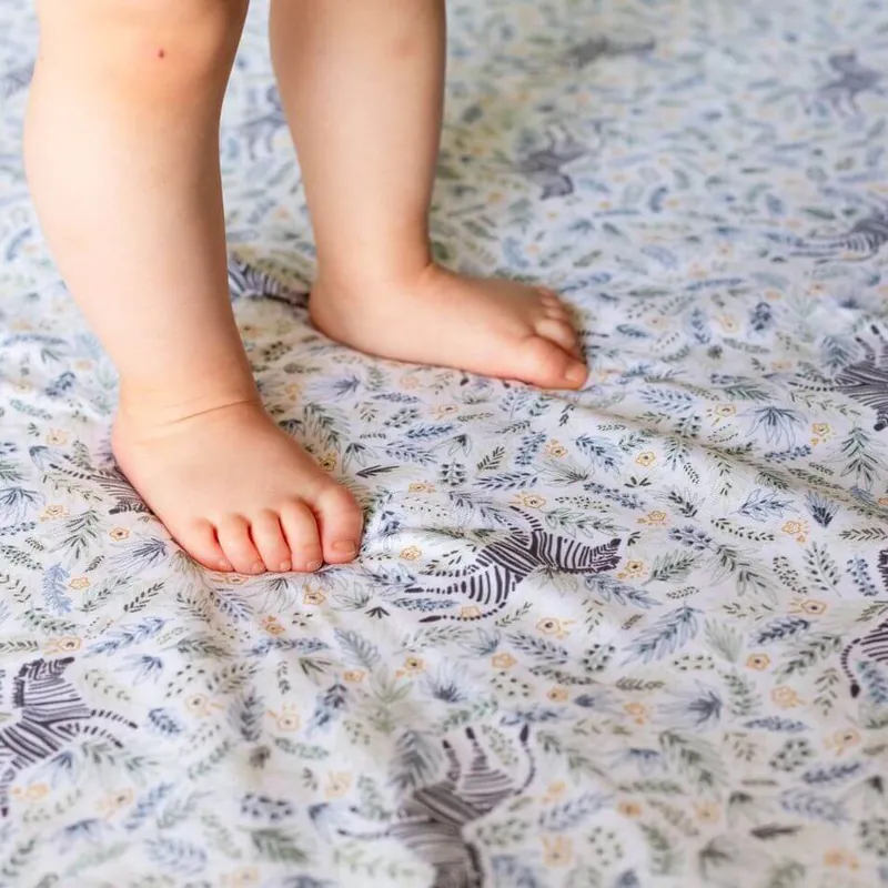 Deux pieds d'enfant nus posés sur un tapis d'éveil blanc imprimé de zèbres et de feuillages