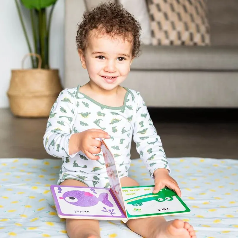 Un petit garçon assis sur un tapis d'éveil imprimé de citrons, qui tourne les pages d'un livre cartonné illustré