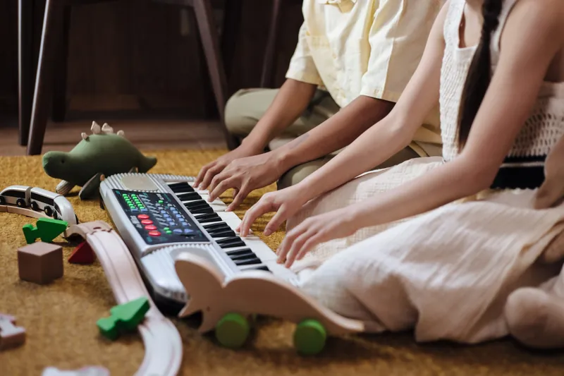 Un adulte et un enfant assis sur un tapis qui jouent ensemble d'un petit clavier, entourés de jouets en bois
