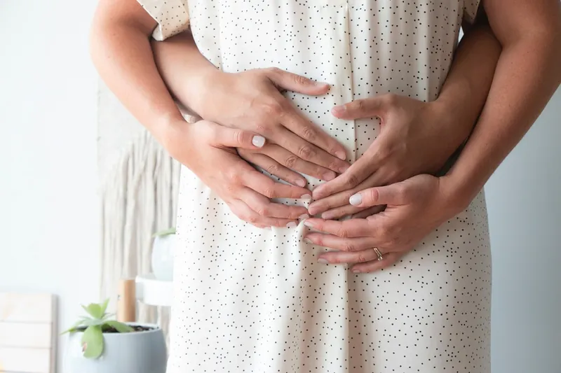 Les mains d'un homme et d'une femme posées ensemble sur le ventre d'une femme enceinte en robe blanche à pois