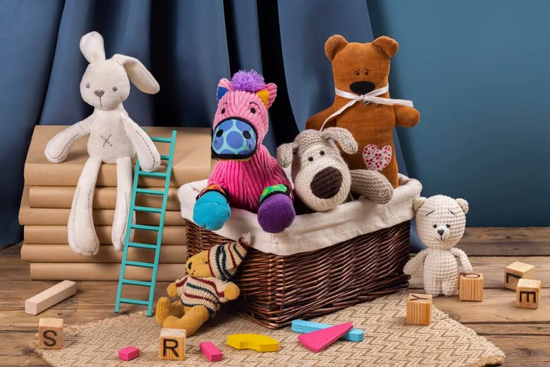 Des peluches et des jouets en bois rangés dans et autour d'un panier en osier, devant un rideau bleu