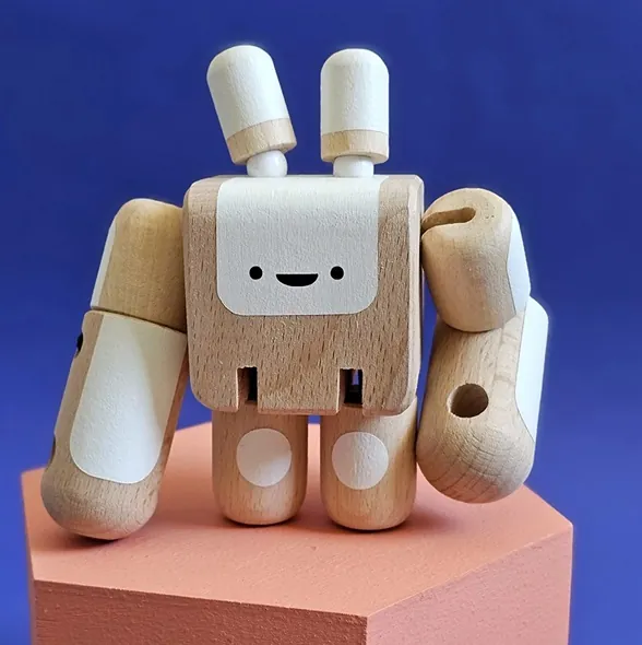 Un robot articulé en bois clair et blanc, au visage souriant, posé sur un socle rose devant un fond bleu
