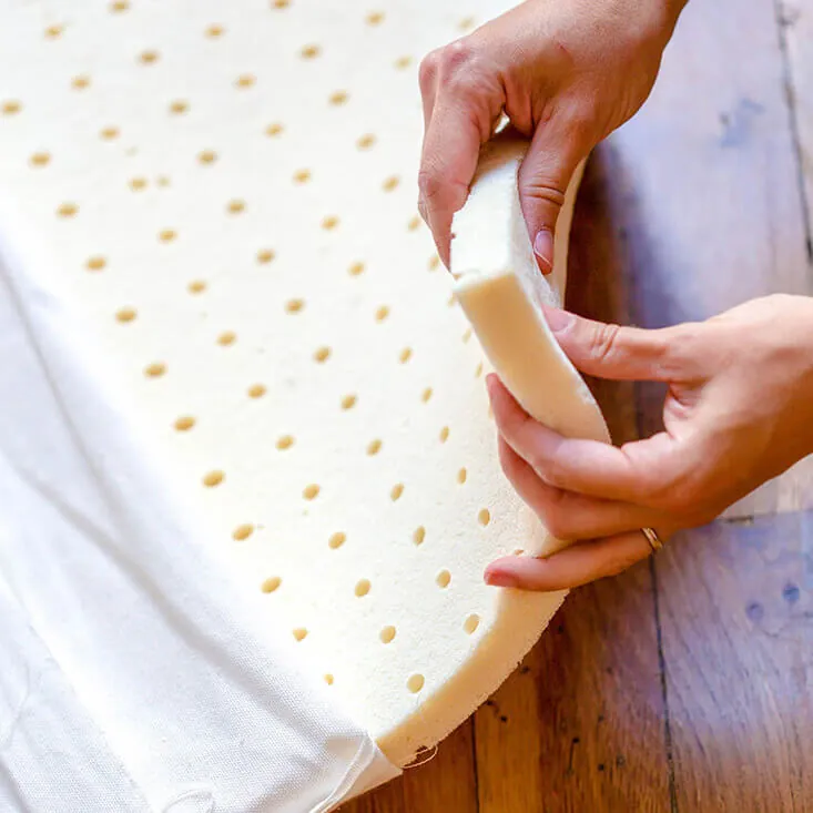 Deux mains qui plient une plaque de mousse de latex naturel perforée, à moitié sortie de sa housse blanche