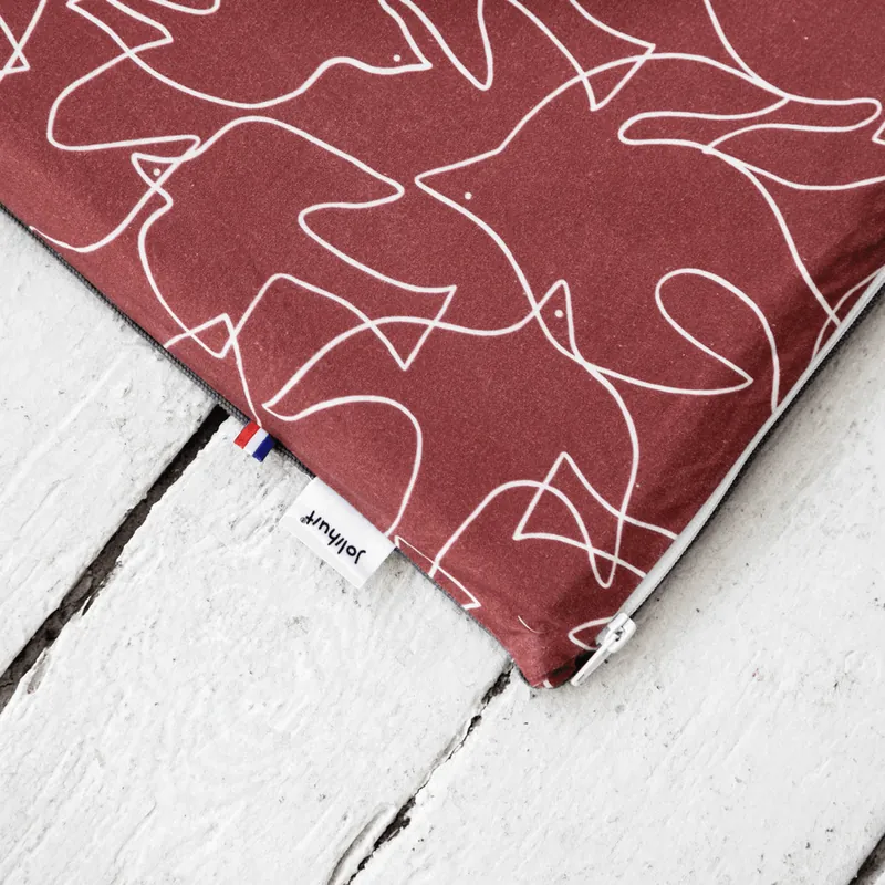 Un tapis d'éveil bordeaux imprimé de silhouettes d'animaux blanches, posé sur un parquet blanc, avec son étiquette Jolihuit