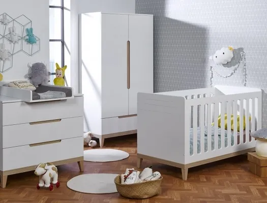 Une chambre de bébé blanche et bois clair : lit à barreaux, commode et armoire