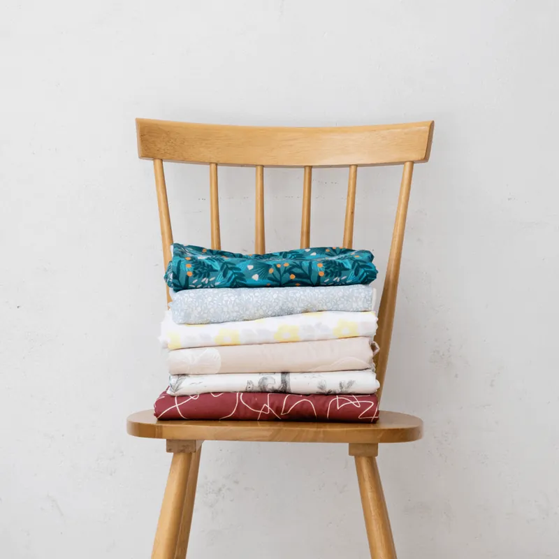 Des housses de tapis d'éveil pliées et empilées sur une chaise en bois, contre un mur blanc